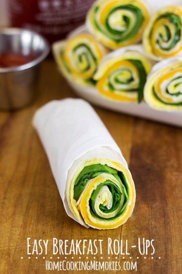 Four breakfast roll up pinwheels with a yellow egg and green spinach spiral, one whole roll up wrapped in paper in front