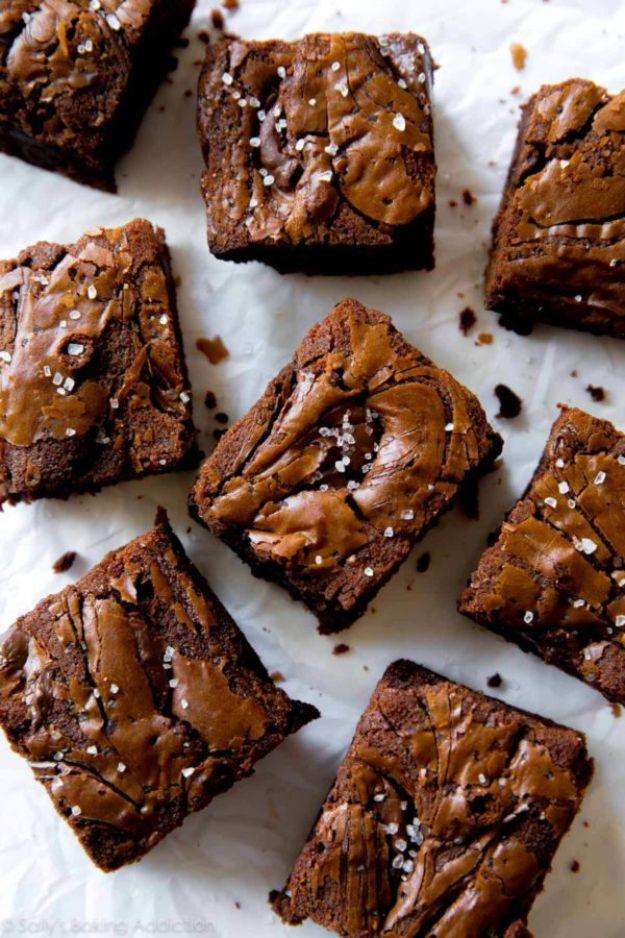 Nutella brownie squares scattered on crinkled white parchment, glossy swirled tops finished with flaky sea salt