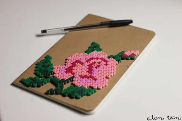 Perler flower notebook, a brown kraft notebook with a beaded pink rose and green leaves, a black pen alongside