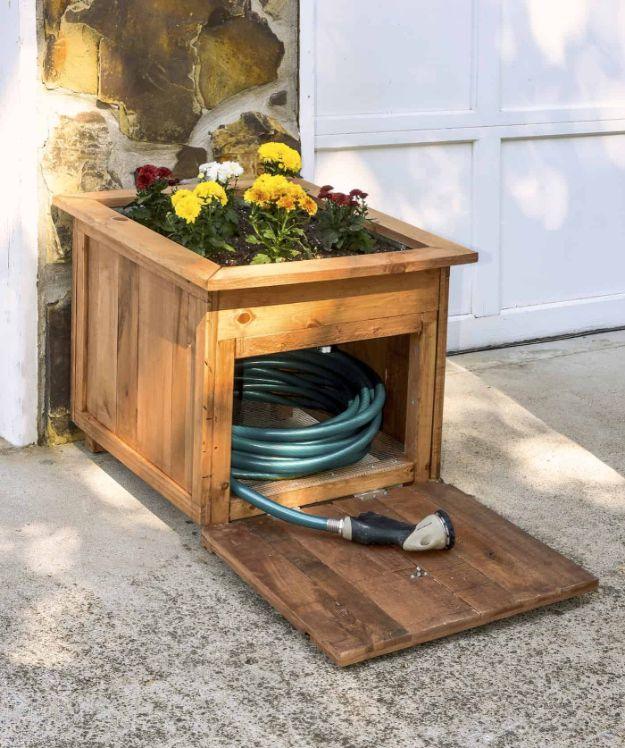 DIY pallet wood hose holder with a planter of marigolds on top, open door showing a coiled green garden hose