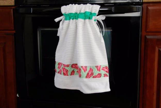 Stay put kitchen towel with a chili pepper print band and a green gathered top, tied onto a black oven handle
