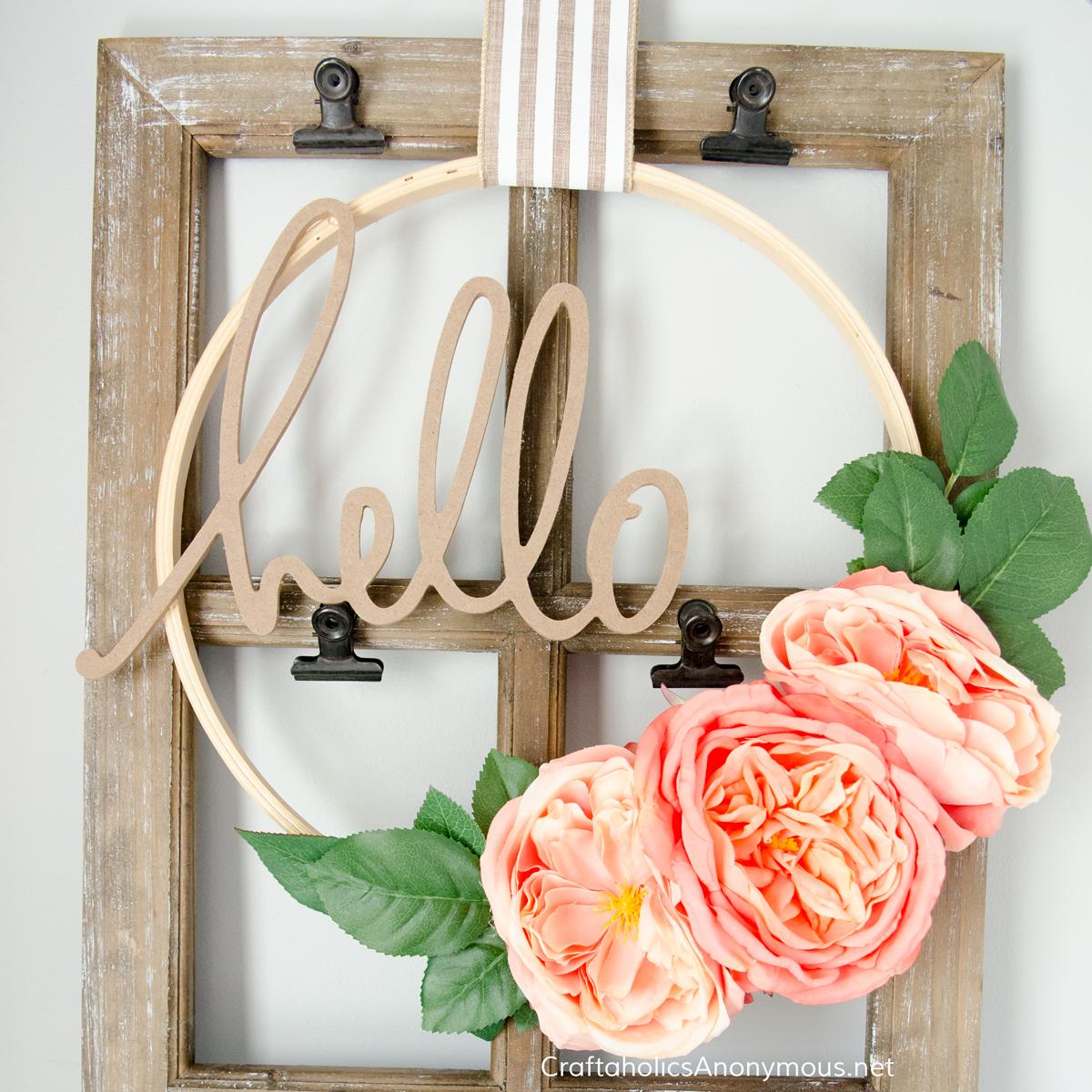 Wood embroidery hoop wreath with three large coral peonies, green leaves and a cut wood hello word on striped ribbon