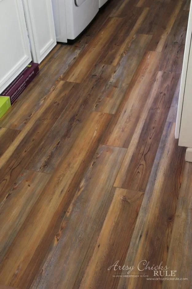 Farmhouse vinyl plank flooring, warm rustic multi-toned planks running through a doorway past white cabinets