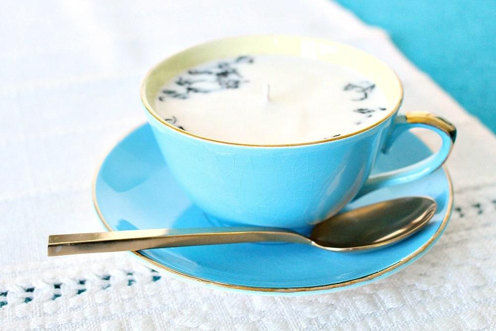 Turquoise vintage tea cup and saucer filled with white soy wax and a wick, with a gold spoon on the saucer