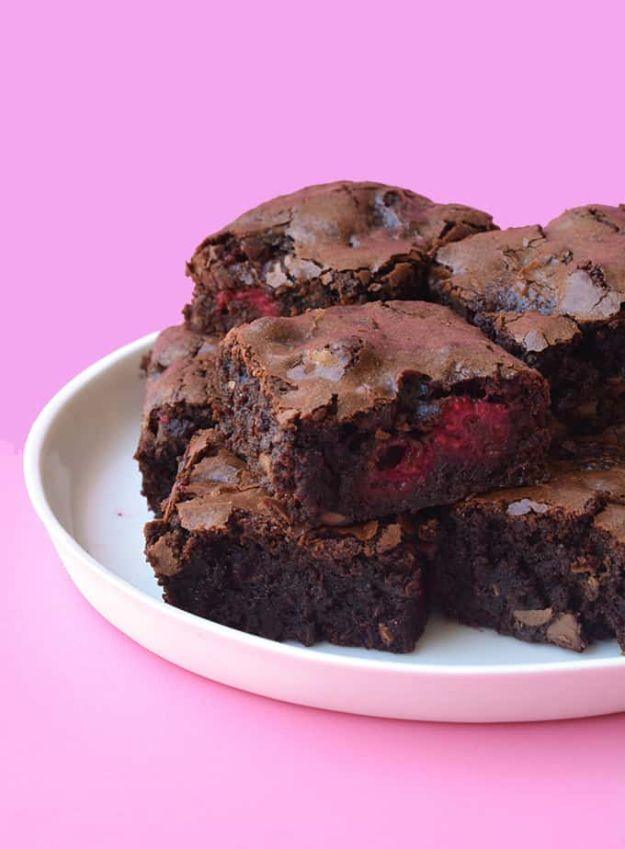 Raspberry chocolate brownies on a white plate against a pink background with whole raspberries baked in