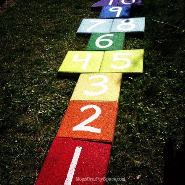 Rainbow paver hopscotch set into a green lawn with concrete squares painted red through purple and numbered in white
