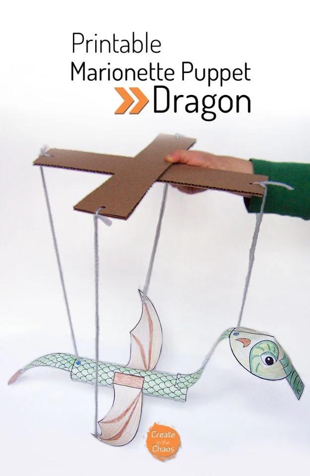 Printable paper dragon marionette hanging on four yarn strings from two crossed cardboard control bars