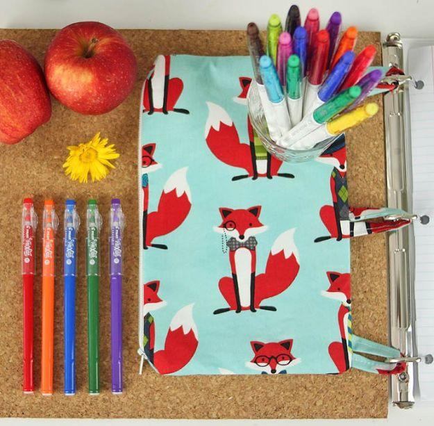 A zip pencil case with metal grommets down one side, clipped into an open three ring binder, sewn in a fun cotton print