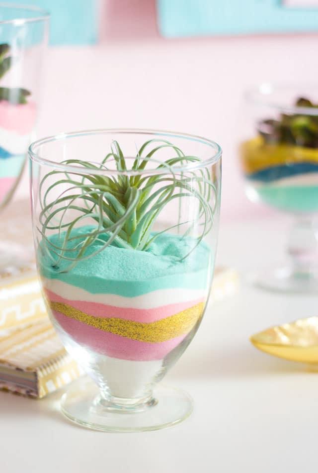 DIY succulent sand art terrariums, a glass with mint pink and gold sand layers topped with a spiky green air plant
