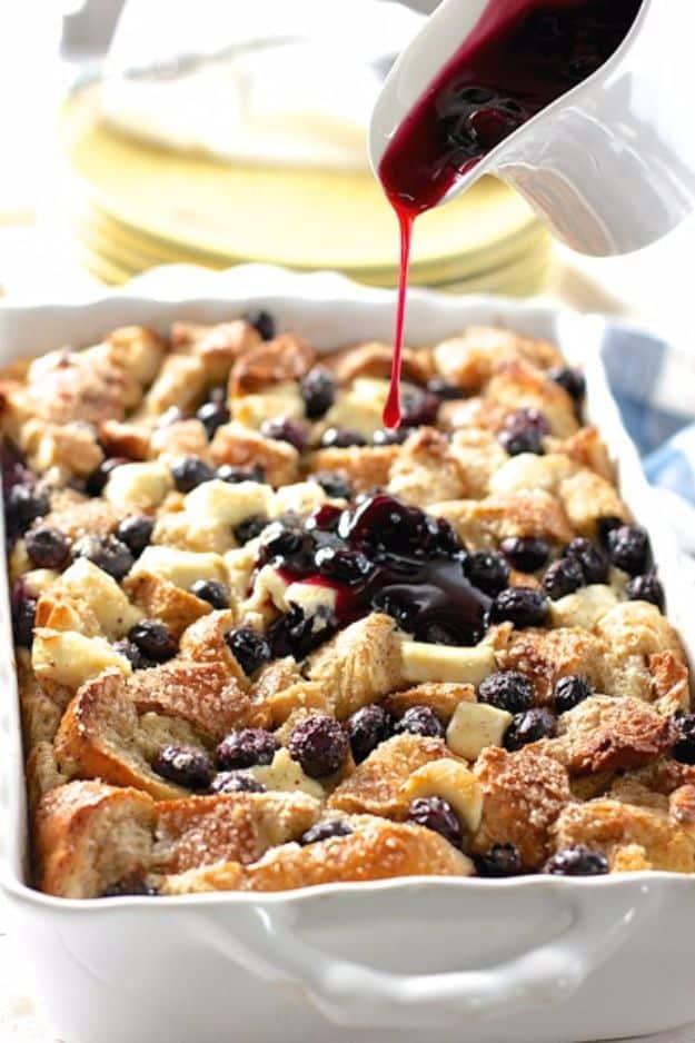 Blueberry and cream cheese french toast casserole in a white dish with blueberry syrup being poured over