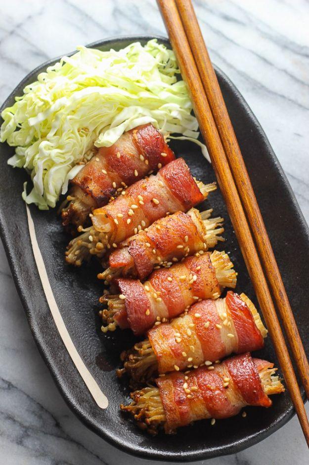 Bacon wrapped enoki mushroom skewers glazed and browned on a black plate with shredded cabbage and chopsticks