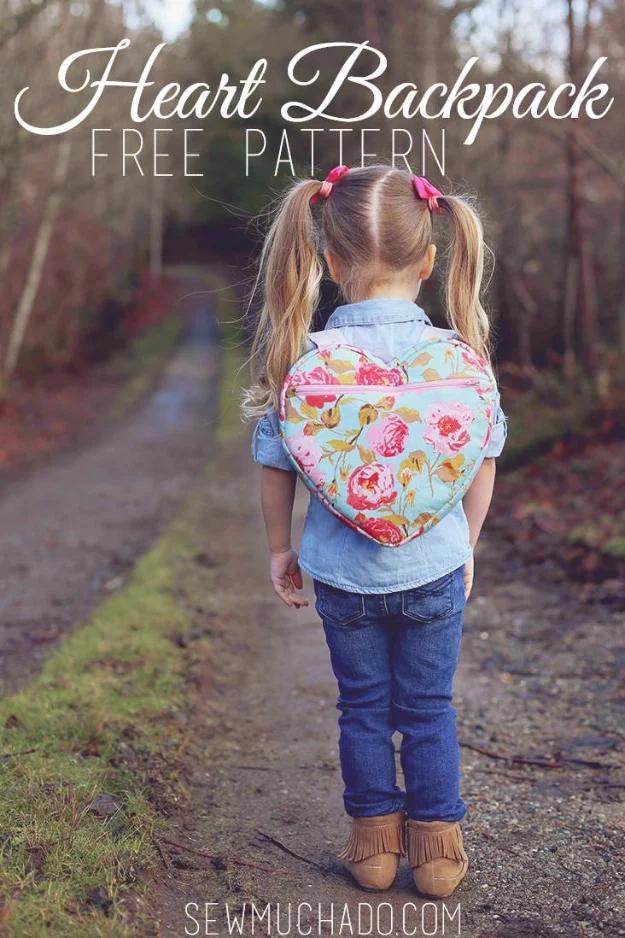 A heart shaped backpack in pink cotton with webbing straps and a zipper, sitting on a child's bedroom floor.