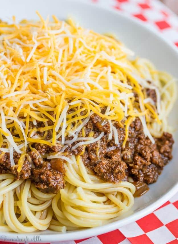Cincinnati chili served over spaghetti and buried under shredded cheddar on a red checked tablecloth