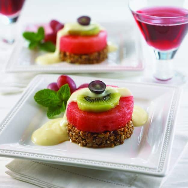 Watermelon benedict, a round of watermelon on a granola base topped with kiwi, yogurt and a dark grape