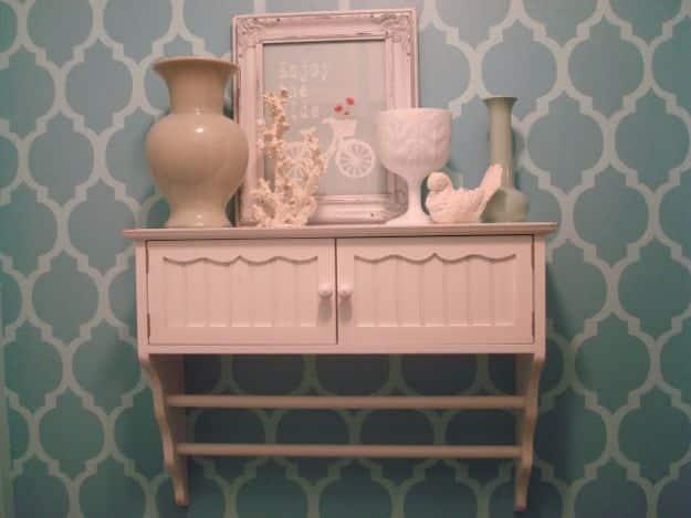 Teal wall stenciled with an allover Moroccan trellis pattern behind a pale pink painted cabinet and vases