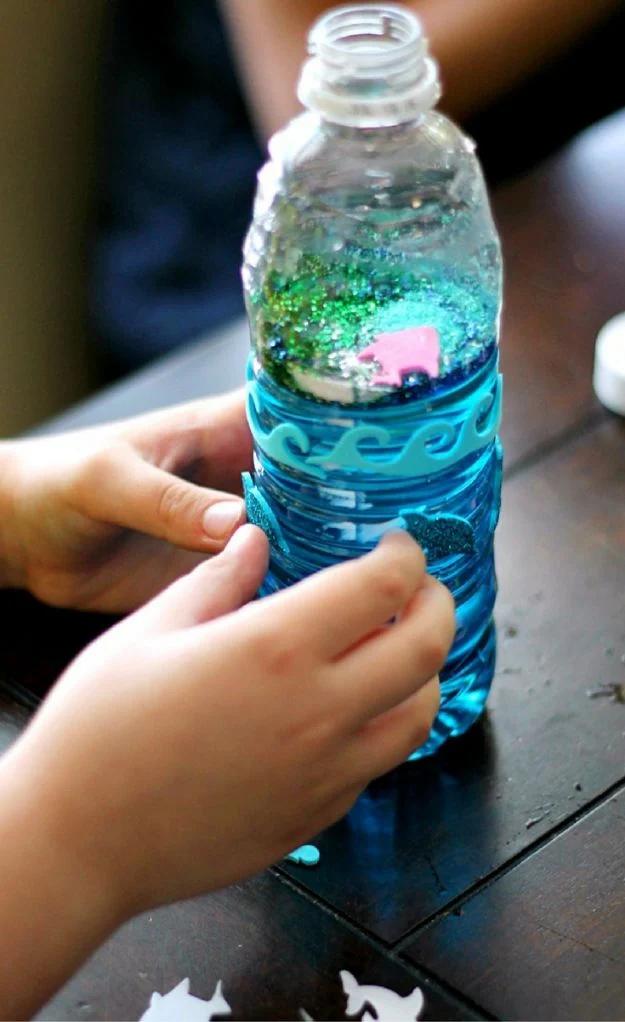 Child pressing foam wave and fish stickers onto a water bottle filled with blue water and green glitter
