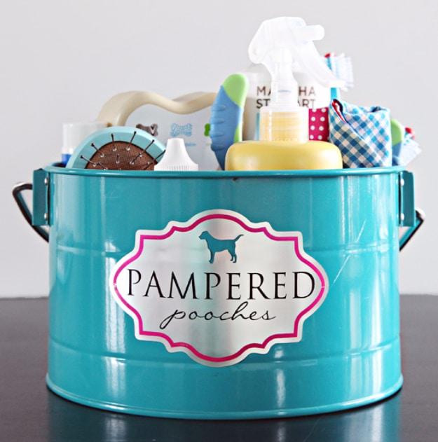 Teal metal bucket caddy labeled Pampered Pooches holding dog brushes, shampoo, a spray bottle and a bandana