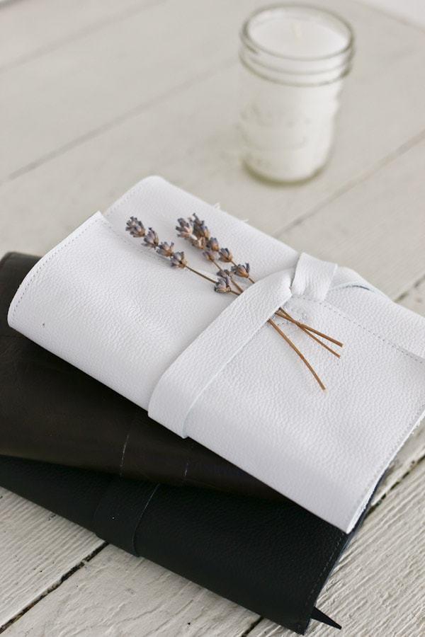 Leather journal covers in white and black wrapped shut with a leather strap and a sprig of dried lavender