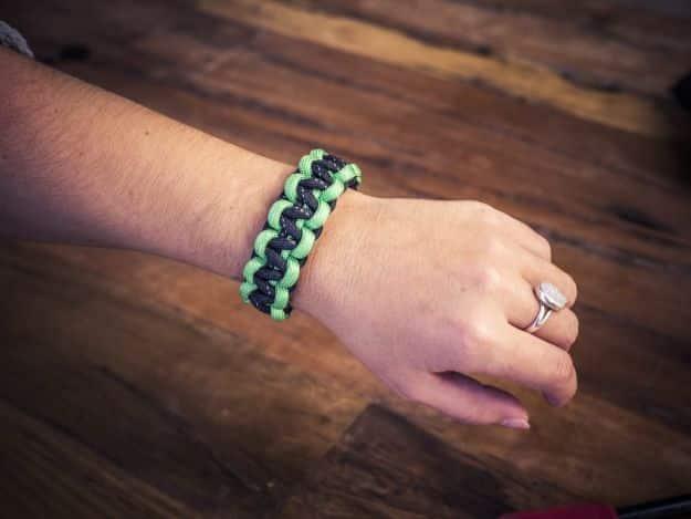 Black and mint green paracord survival bracelet in a narrow cobra weave, worn on a wrist over a wood table