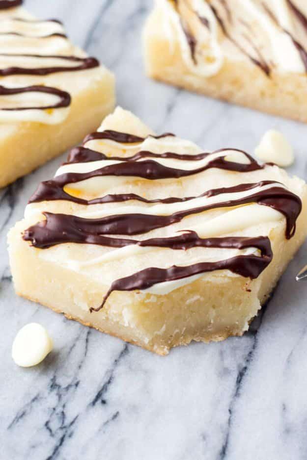 White chocolate brownies on marble with a pale golden crumb and dark chocolate drizzled over the top