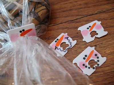 Three plastic bread tags painted as snowman faces with orange noses, one clipped onto a cellophane treat bag