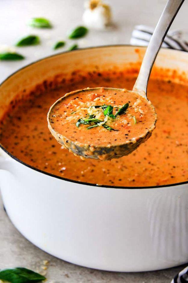 Creamy tomato basil soup being ladled from a white pot, flecked with pepper and a little chopped basil