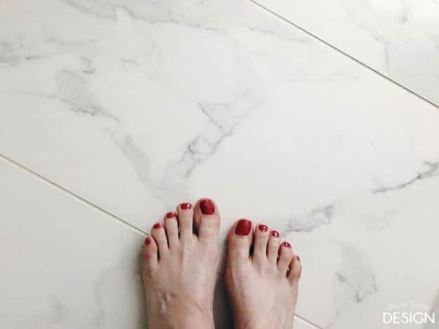 Heated floors, bare feet with red polish standing on white marble look porcelain tile over an underfloor heating system
