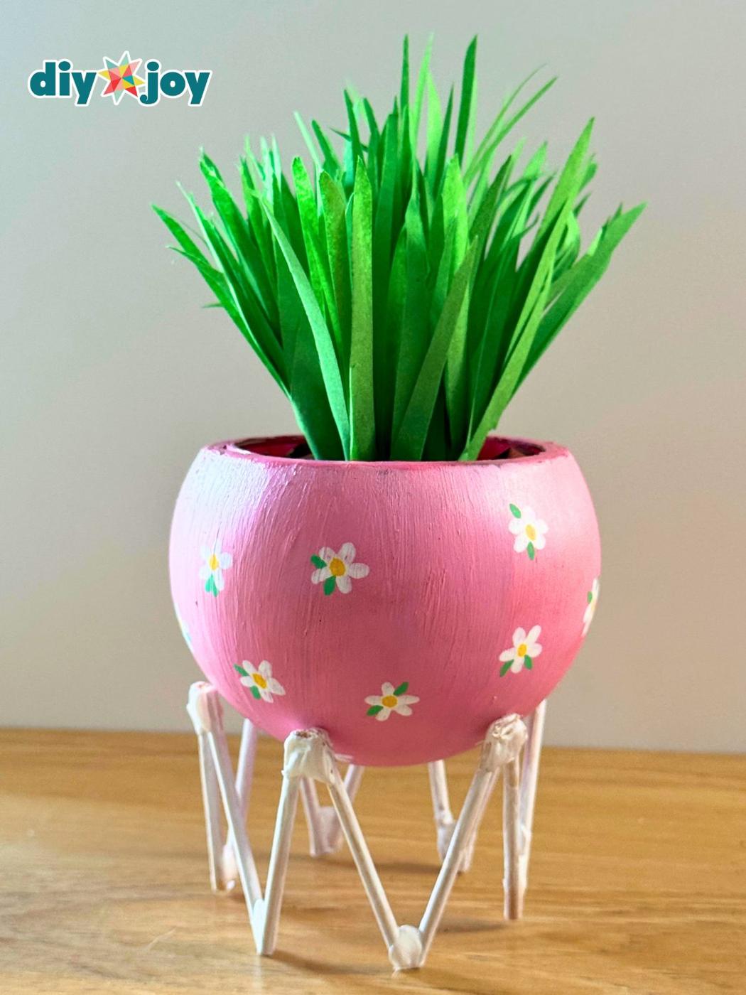 Pink painted light bulb planter with white daisies and green paper grass standing on a ring of craft sticks
