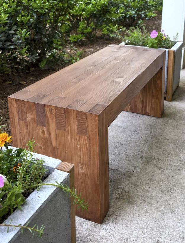 Modern DIY outdoor bench in warm stained pine with interlocking box joint ends, on concrete beside planter boxes