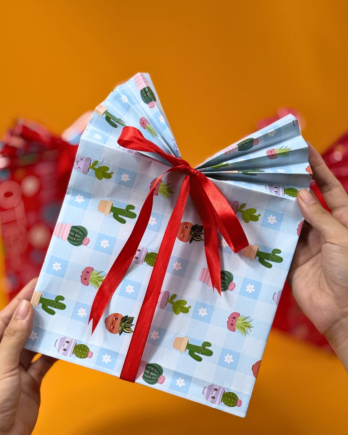 Christmas Gift Wrapping - hands holding a light blue cactus print paper gift bag with a red ribbon bow
