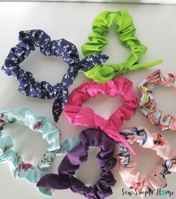 Six fabric scrunchies in navy, lime green, pink, purple and mint spread out on a white background in a loose pile