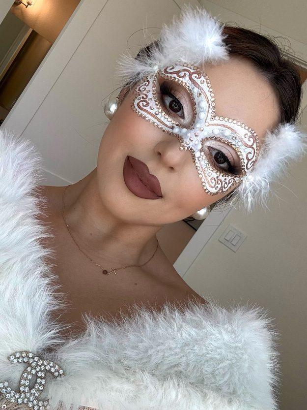 Masquerade Halloween makeup with a silver mask painted around the eyes, rhinestones and white feathers