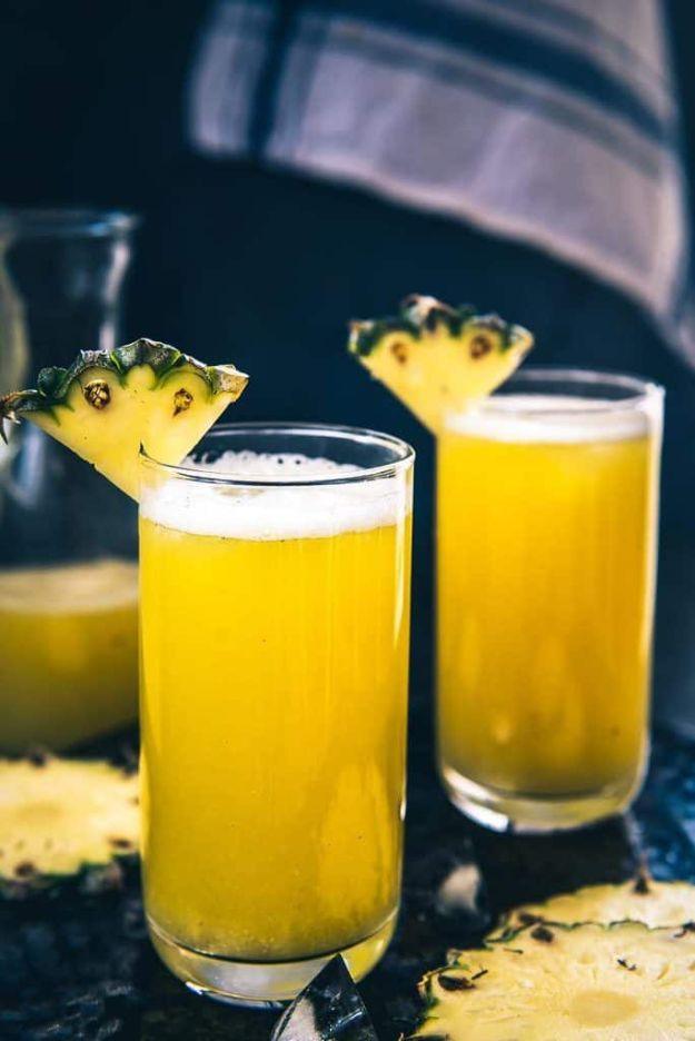 Homemade fresh pineapple juice in two tall glasses with pineapple wedges on the rims against a dark backdrop