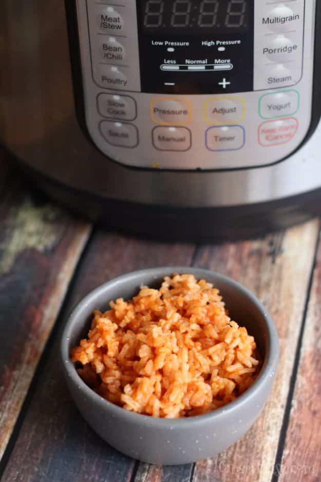 Small grey bowl of red Mexican rice on a wood table with the control panel of an instant pot behind it