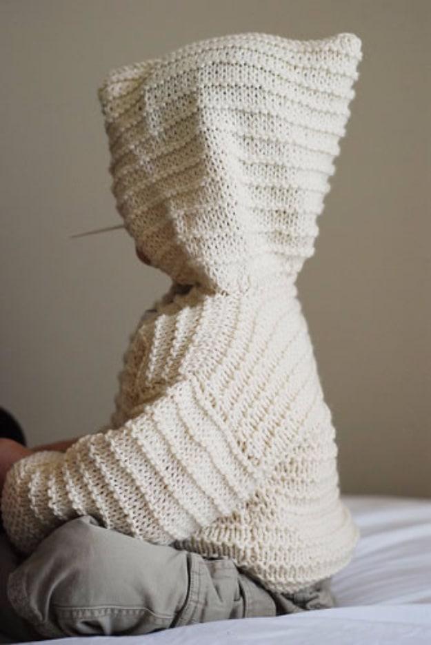 Cream knitted baby hoodie with garter ridge stripes worn by a small child lying down, face not visible