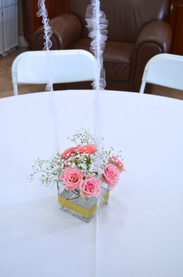 DIY baby shower decoration centerpiece with pink roses and gypsophila in a gold banded square vase on a white table