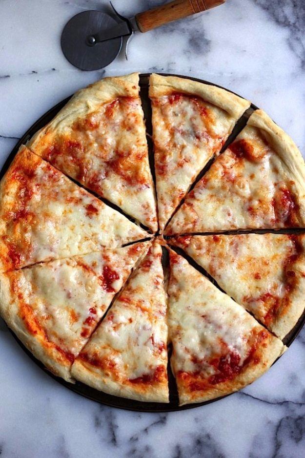 Round New York style cheese pizza cut into eight even slices on white marble beside a metal pizza wheel