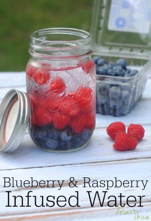 Blueberry and raspberry infused water in an eight ounce canning jar beside fresh berries and the open lid