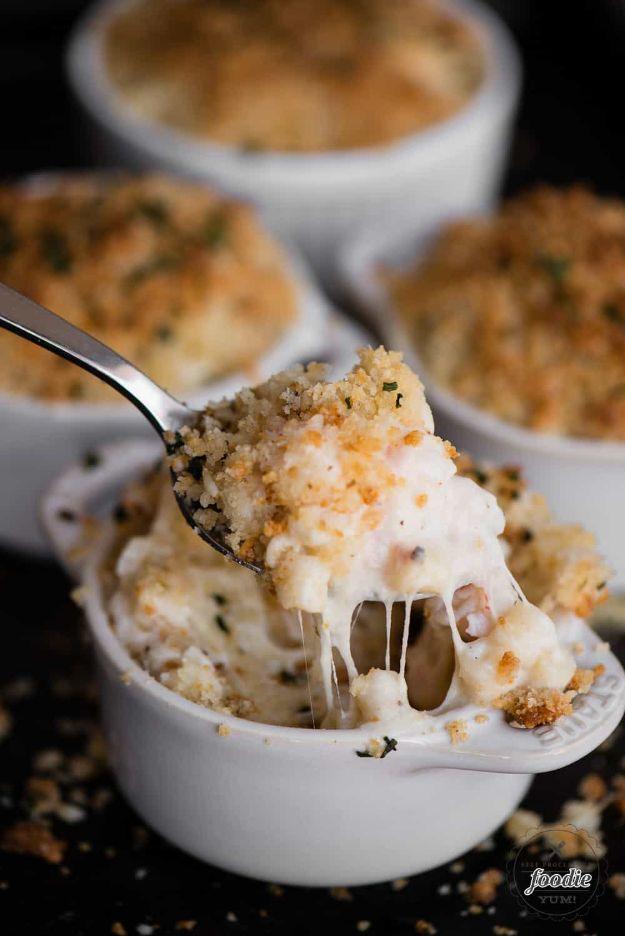 Lobster mac and cheese baked in white ramekins with a spoon lifting a cheesy bite from a panko topped portion