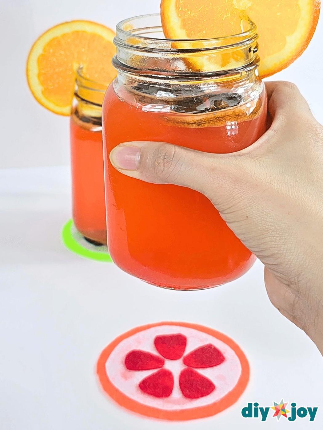 Felt fruit coasters shaped like a lemon, a watermelon slice and an apple with a glass of orange juice on one