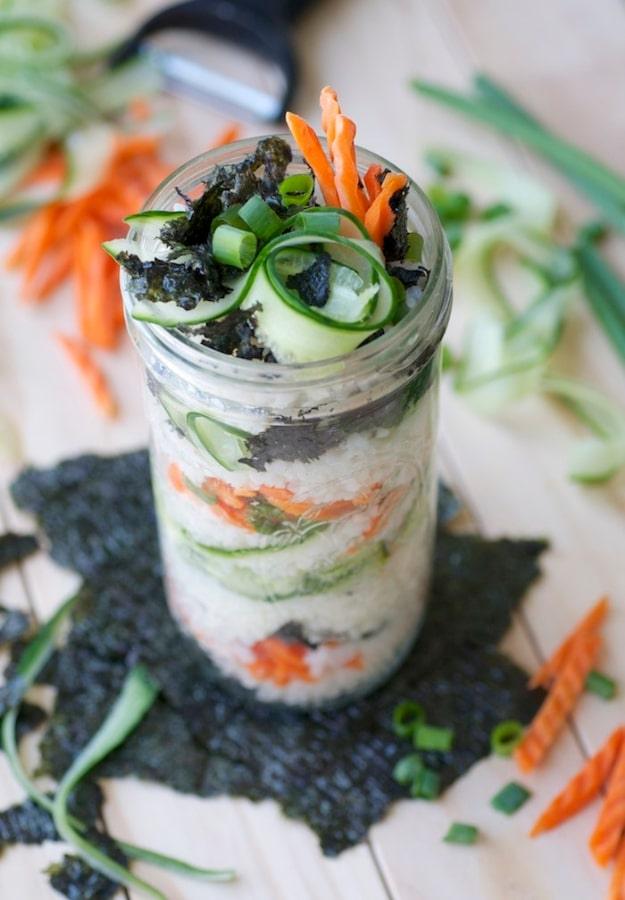 Sushi in a jar layered with seasoned sushi rice, carrot, cucumber ribbons, green onion and torn nori sheets