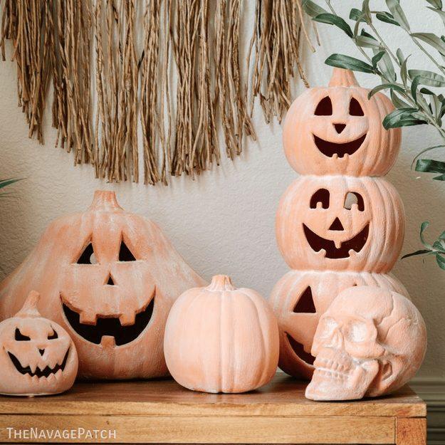Plastic jack-o-lantern pumpkins and a skull painted to look like aged terracotta, stacked on a wood console