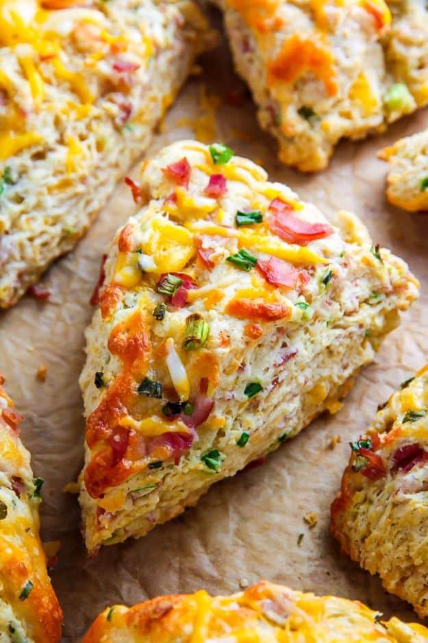 Ham and cheese scones on parchment, triangular wedges topped with melted cheddar, ham pieces and scallions