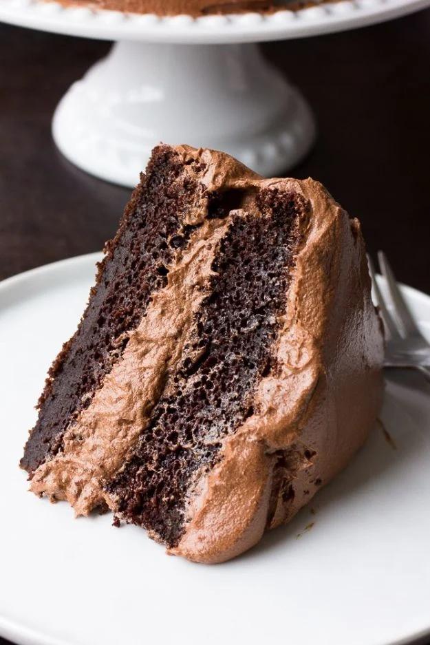 Thick slice of two layer vegan chocolate cake with chocolate buttercream on a white plate beside a fork