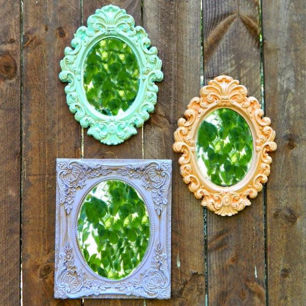 Three ornate plastic frames painted mint, lavender and peach, hung on a weathered wood fence with greenery inside