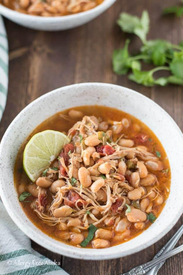 Instant pot white bean chicken chili in a white bowl with a lime wedge and cilantro on a dark wood table