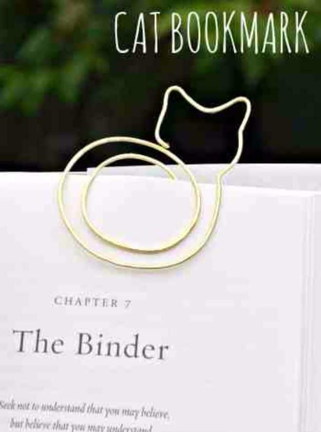 DIY cat bookmark, a gold wire cat with a spiral body clipped over the printed pages of an open hardback book
