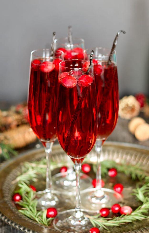Four champagne flutes of red vanilla cranberry mimosa on a tray, each garnished with a whole vanilla bean