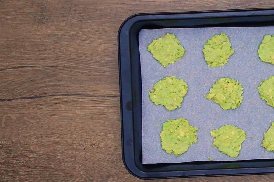 Small mounds of avocado mixture spooned onto a lined baking tray before baking