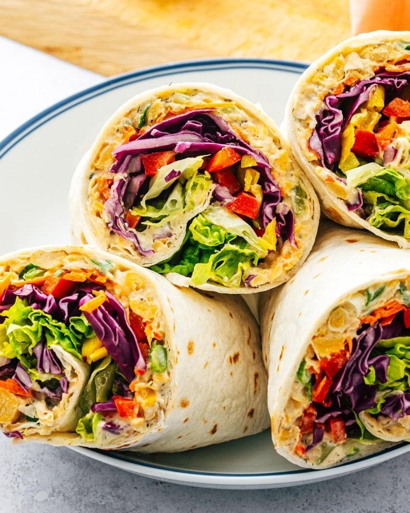 Healthy veggie wrap halves showing red cabbage, peppers, carrot and lettuce rolled in a flour tortilla